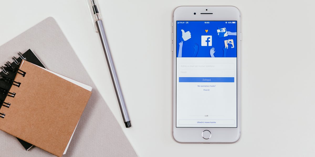 Smartphone with Facebook on screen beside notebooks and pen